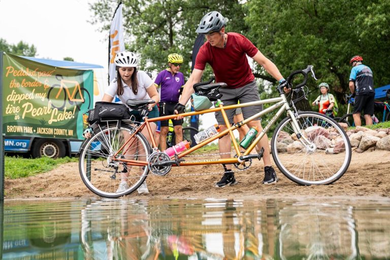 Danielle Fineza, left, and Alex Ei, right, from Ames, Iowa, dip their ties into Pearl Lake during Day Two of RAGBRAI 52 on July 21, 2025, at Brown Park in Jackson, Minn.